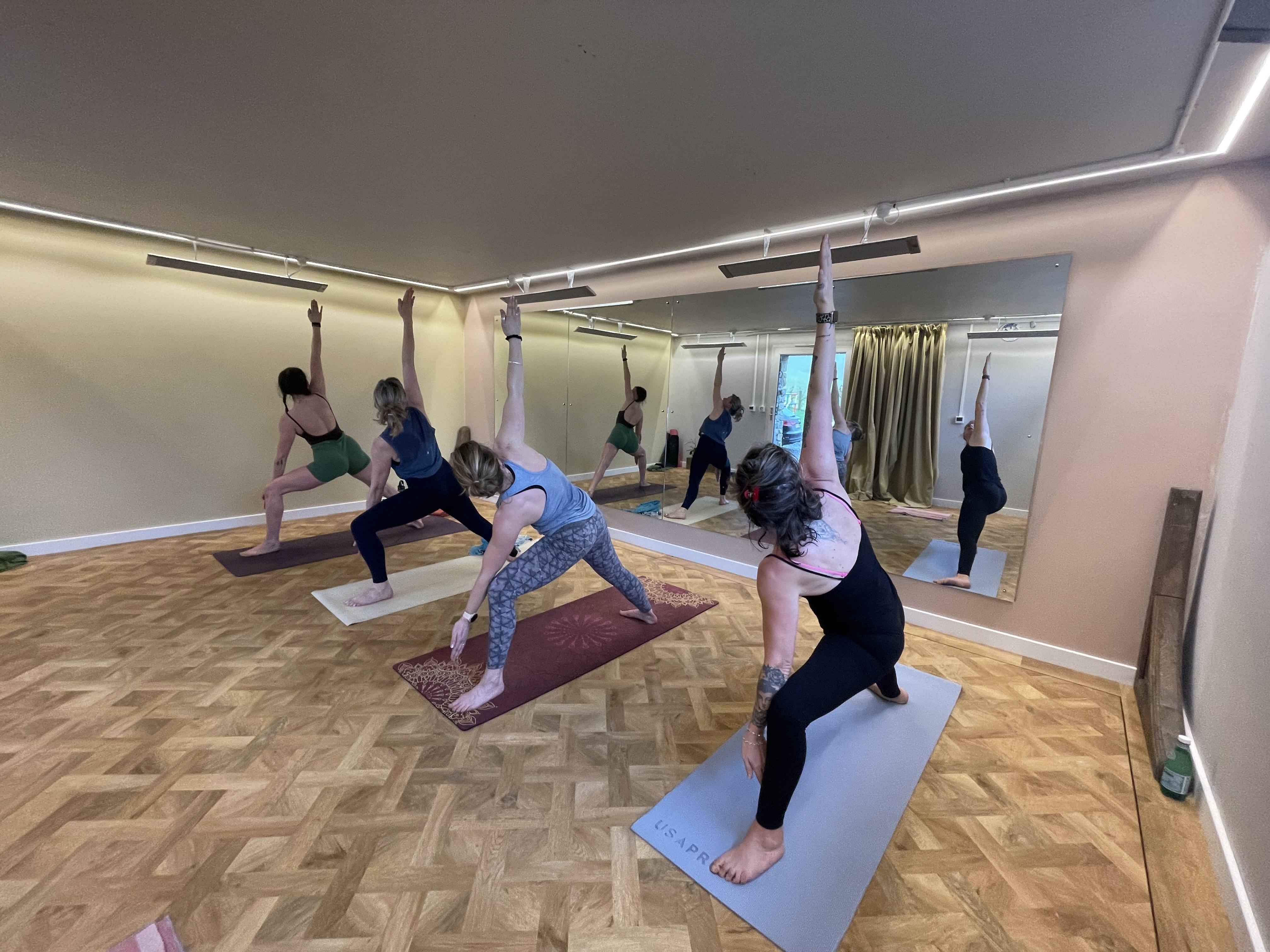 Hot yoga class in session at Hot Yoga Cumbria — students in warrior pose on the parquet studio floor