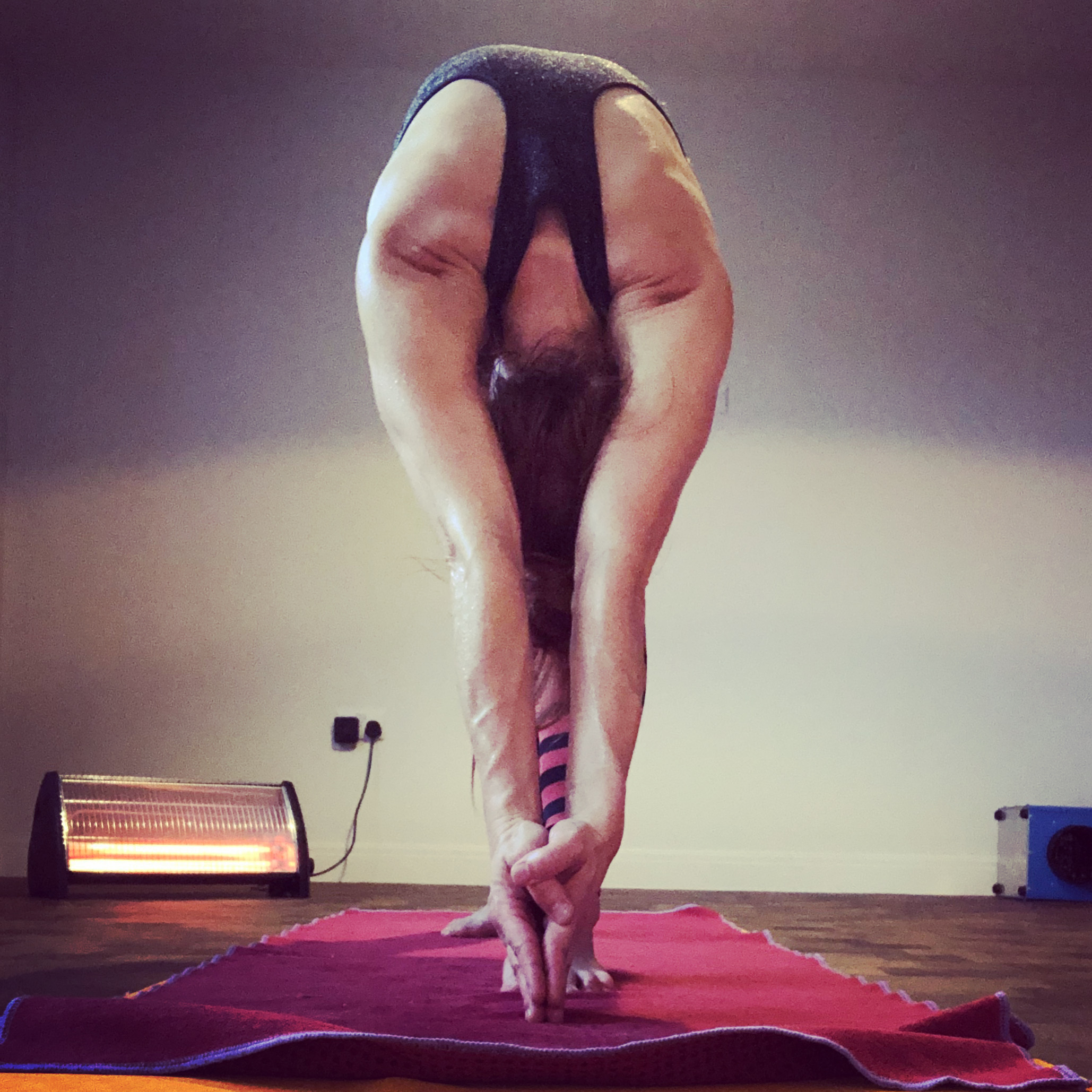 Deep forward fold in the heated studio at Hot Yoga Cumbria — the studio heater visible in the background